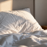 Insomnia Drug Helps People Fall Asleep Faster and Stay Asleep Longer in Clinical Trial Simple natural photograph of rumpled white bedding and a bedside alarm clock in gentle morning light
